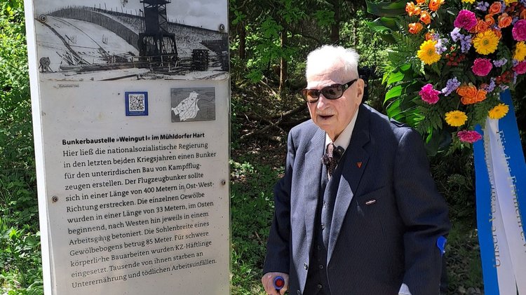 Mann mit Gehhilfen an einer beschrifteten Stele: Gedenkakt im Rahmen des bayerisch-französischen Gedenkprojekts „Den französischen Opfern des KZ Mühldorf in memoriam“ anlässlich 80 Jahre Befreiung des Mühldorfer Außenlagers des KZ Dachau.  