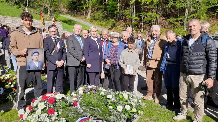 Niedergelegte Kränze und Personengruppe mit Bildern: Gedenken anlässlich des 80. Jahrestages der Befreieung des Konzentrationslagers. Bezirksgeschäftsführer Dr. Dario Vidojkovic (Zweiter von links) mit Vertretern der Generalkonsulate der Republik Kroatien, der Republik Slowenien und Angehörigen der Opfer aus Slowenien und Montenegro. 